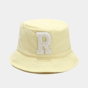 Close-up of a pale yellow bucket hat featuring a white chenille letter R patch texture