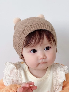 Cute knitted baby winter hat with pom-poms and ear protection in light coffee color