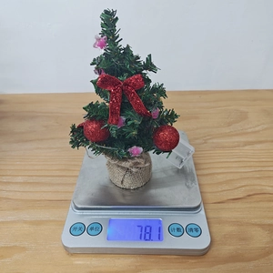 Close-up of a mini Christmas tree featuring red bows and rustic burlap base weighed on scale