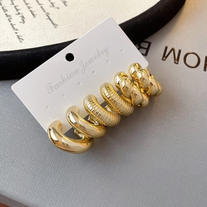 Three pairs of golden C-shaped hoop earrings in chunky and ribbed styles on a white card