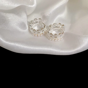 Detailed macro view of silver crown earrings with delicate pearl trim on white silk