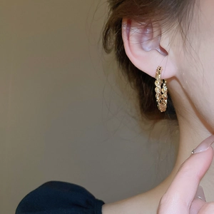 Close-up of gold-plated twisted hoop earrings with woven texture on a model