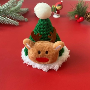 Detail of green knitted pet Christmas hat with reindeer doll on festive red background