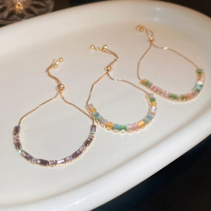 Adjustable gold bracelets with colorful rectangular zircons on a white ceramic tray