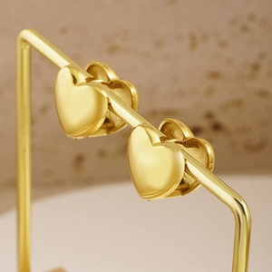 Polished gold heart-shaped earrings on a display stand, minimalist fashion jewelry for women