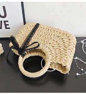Detail of a woven straw handbag featuring black lace bows and a round integrated handle