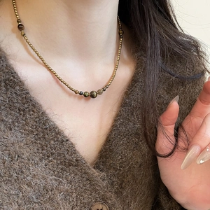 Detail of tiger eye beaded necklace on model with golden metal accents and vintage look