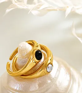 Detail shot of gold open rings with black gemstone and white pearl on a white shell