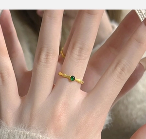 Detail of a gold bamboo-style ring with a green gemstone on a model's hand