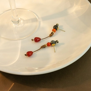 Detail of beaded tassel earrings in red and grey on white ceramic plate with soft lighting