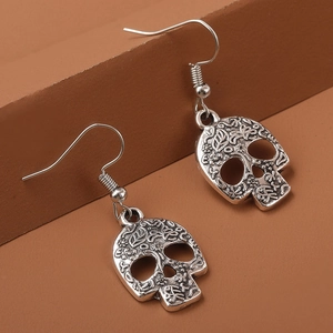 Macro shot of silver skull earrings with detailed floral engraving on brown steps