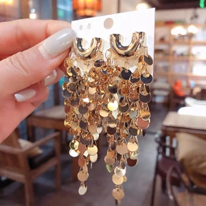 Close-up of golden fan-shaped tassel earrings with tiered metal sequins on U-shaped studs