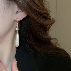 Détail de boucles d'oreilles pendantes dorées avec zircon et perles sur un mannequin