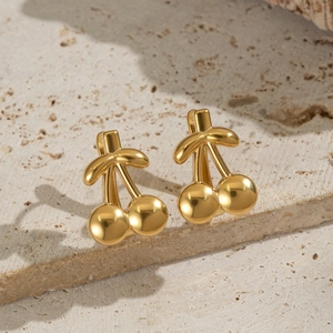 Detail of 18K gold-plated cherry stud earrings on a natural stone textured surface
