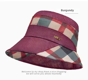 Detail of burgundy plaid sun hat featuring a gold LOVE metal emblem on a breathable fabric