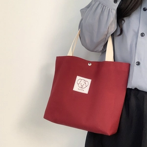 Detail of burgundy canvas tote bag featuring a cute cartoon dog label and white tag