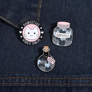 Detail of three cartoon cat enamel pins featuring Pawsitive Vibes text on denim