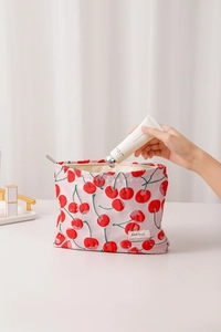 Detail of red cherry print canvas makeup bag being used on a clean white desk