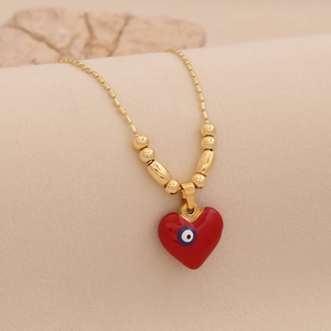 Collier chaîne dorée à billes avec pendentif cœur rouge et œil bleu sur fond beige