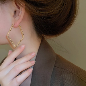 Detail of large golden geometric diamond earrings with textured surface worn by model