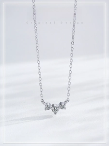 Vertical view of a delicate silver necklace with three aligned crystals on white silk