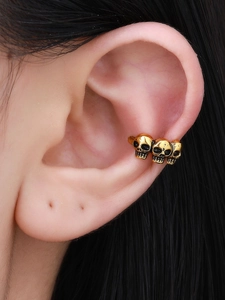 Macro shot of punk style golden ear cuff featuring three skulls on a model's ear cartilage