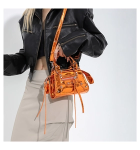 Orange patent leather motorcycle bag with silver studs and tassel detail on black jacket