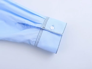 Détail de la manchette d'une chemise bleu clair avec surpiqûres noires et bouton blanc