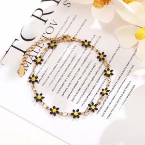 Detailed macro view of daisy enamel charms on gold-plated stainless steel chain bracelet