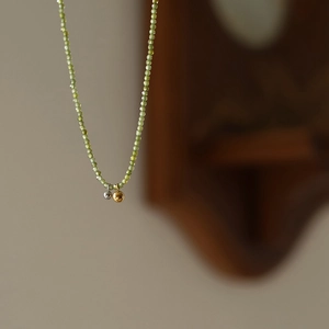 Olive green beaded necklace with gold and silver ball pendants on a vintage wood background