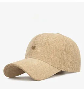 Detail of beige herringbone baseball cap featuring a gold heart-shaped metal emblem