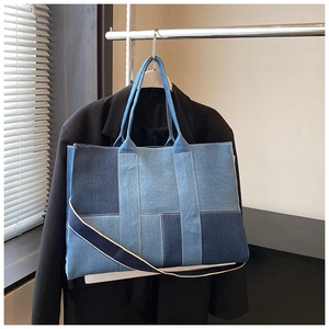 Detail of blue patchwork denim tote bag hanging on a hanger with wide shoulder strap