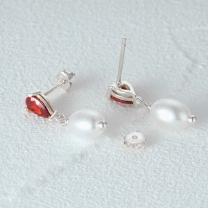 Macro shot of S925 sterling silver earrings with pear-cut ruby and white pearl drop