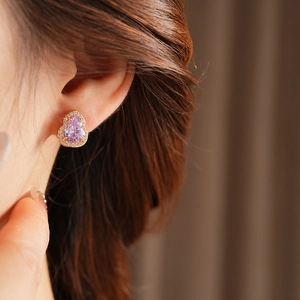 Close-up of gold-plated gourd earrings with purple zircon gemstone worn by a model