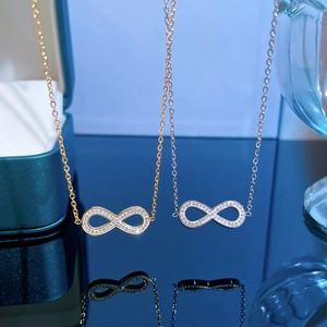 Gold and silver infinity symbol necklaces with cubic zirconia on a reflective surface