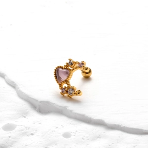 Detailed macro shot of a heart-shaped gold cartilage stud with purple zircon on white stone