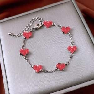 Detail of red heart charms on golden metal chain bracelet lying on silk fabric
