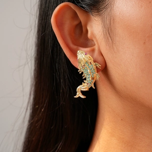 Detail view of a gold koi fish earring inlaid with blue and pink crystals on a model's ear
