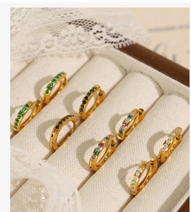 Macro detail of gold plated huggie earrings with colorful zirconia in a velvet box