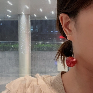 Close-up of stylish red cherry earrings with gold hooks worn by a model in a lifestyle setting