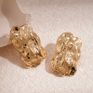 Detailed macro view of golden metallic wrinkled geometric stud earrings on stone texture