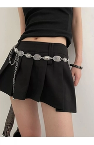 Detail of Y2K silver metal belt with oval embossed links on black pleated mini skirt