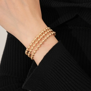 Dettaglio del bracciale a tre strati con perle in oro 18K su polso con sfondo in maglia nera