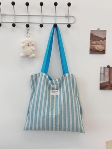 Dettaglio della borsa tote in tela a righe blu con tracolla azzurra e toppa del logo