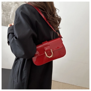 Detail of red patent leather shoulder bag with gold horseshoe buckle on black coat