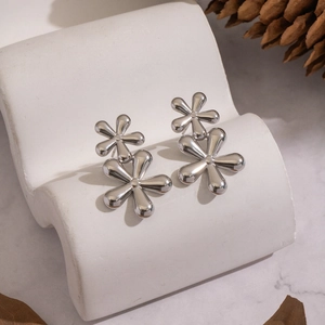 Macro detail of silver double-layered flower earrings on a white elegant display stand