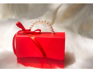 Detail of red wedding candy box with pearl handle, ribbon bow and embossed patterns