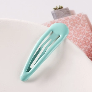 Detail of a mint green water drop metal hair clip resting on a white ceramic plate