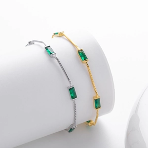 Detailed view of gold and silver box chain bracelets with emerald cut green gemstones