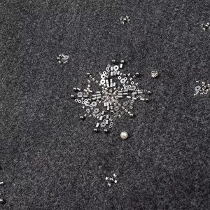 Vista macro di paillettes argentee e ricami di perle su giacca grigia
